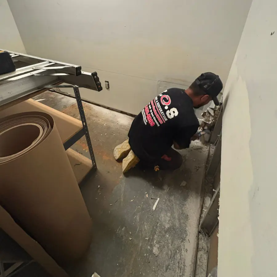 Technician in PPE flood-cutting water-damaged drywall in the basement