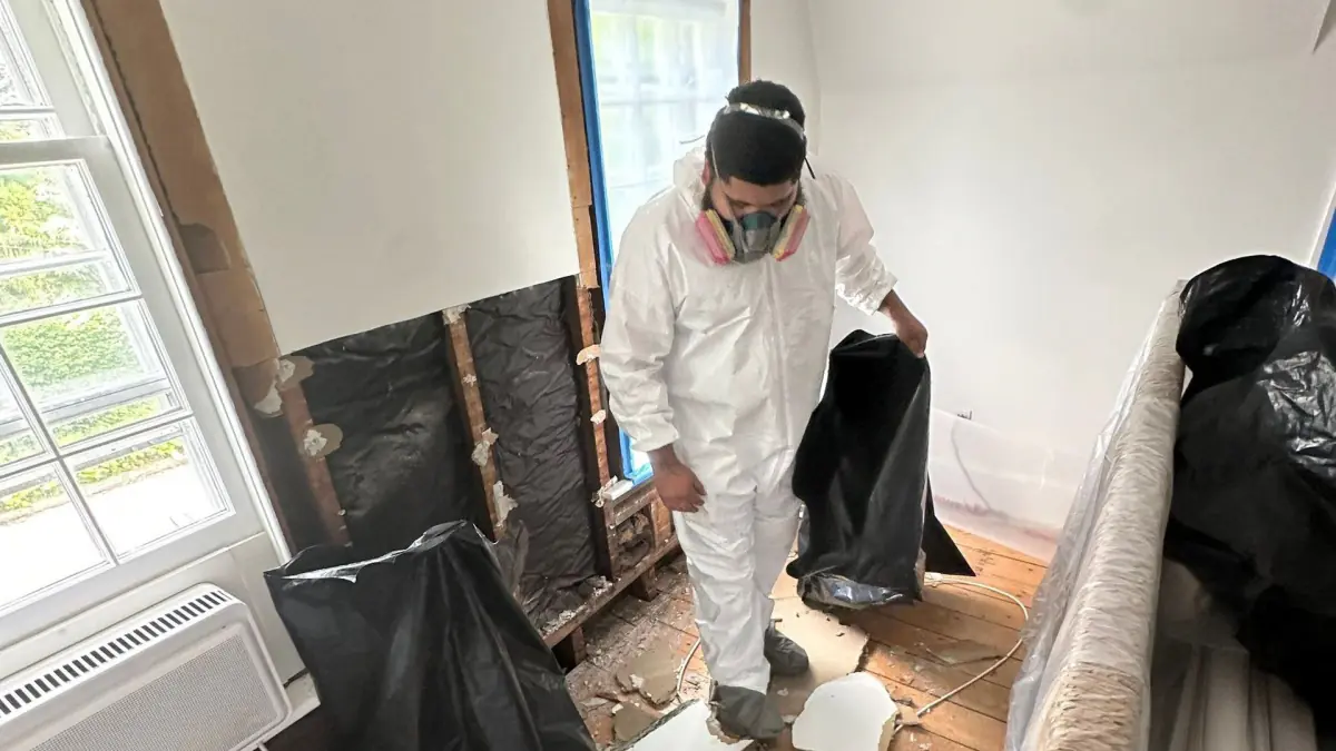 Technician in PPE bagging water-damaged drywall in a Sag Harbor bedroom