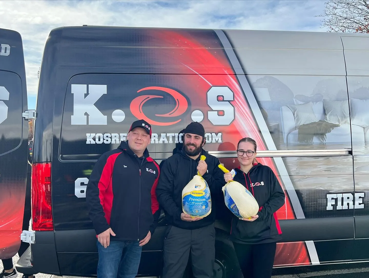 Three K.O.S. Restoration crew members holding donated turkeys in front of the van