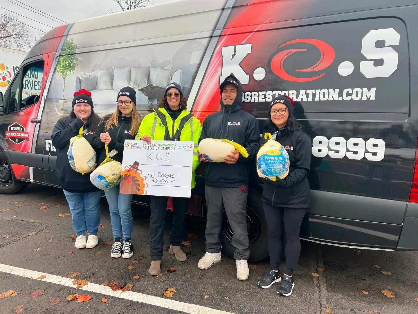 K.O.S. Restoration team holding turkeys and a sign for 50 turkeys and $2,500 beside a company van