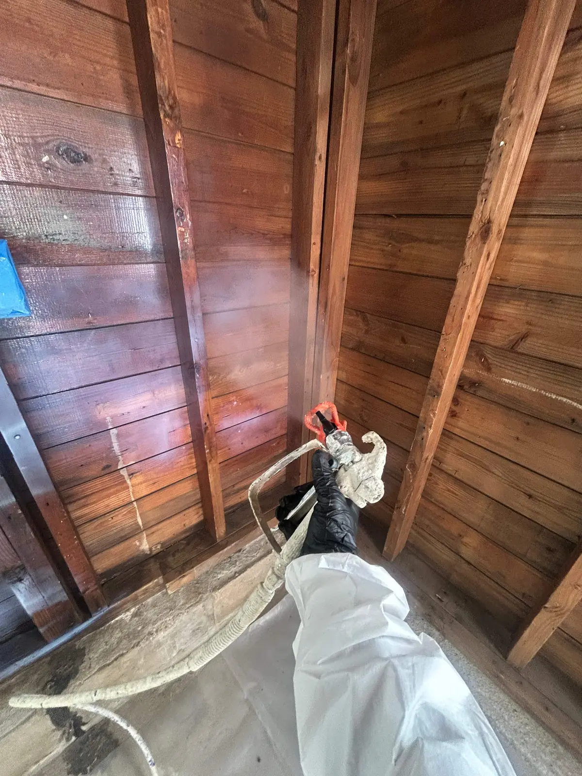 Technician in a protective suit cleaning soot off the wall boards with a spray wand