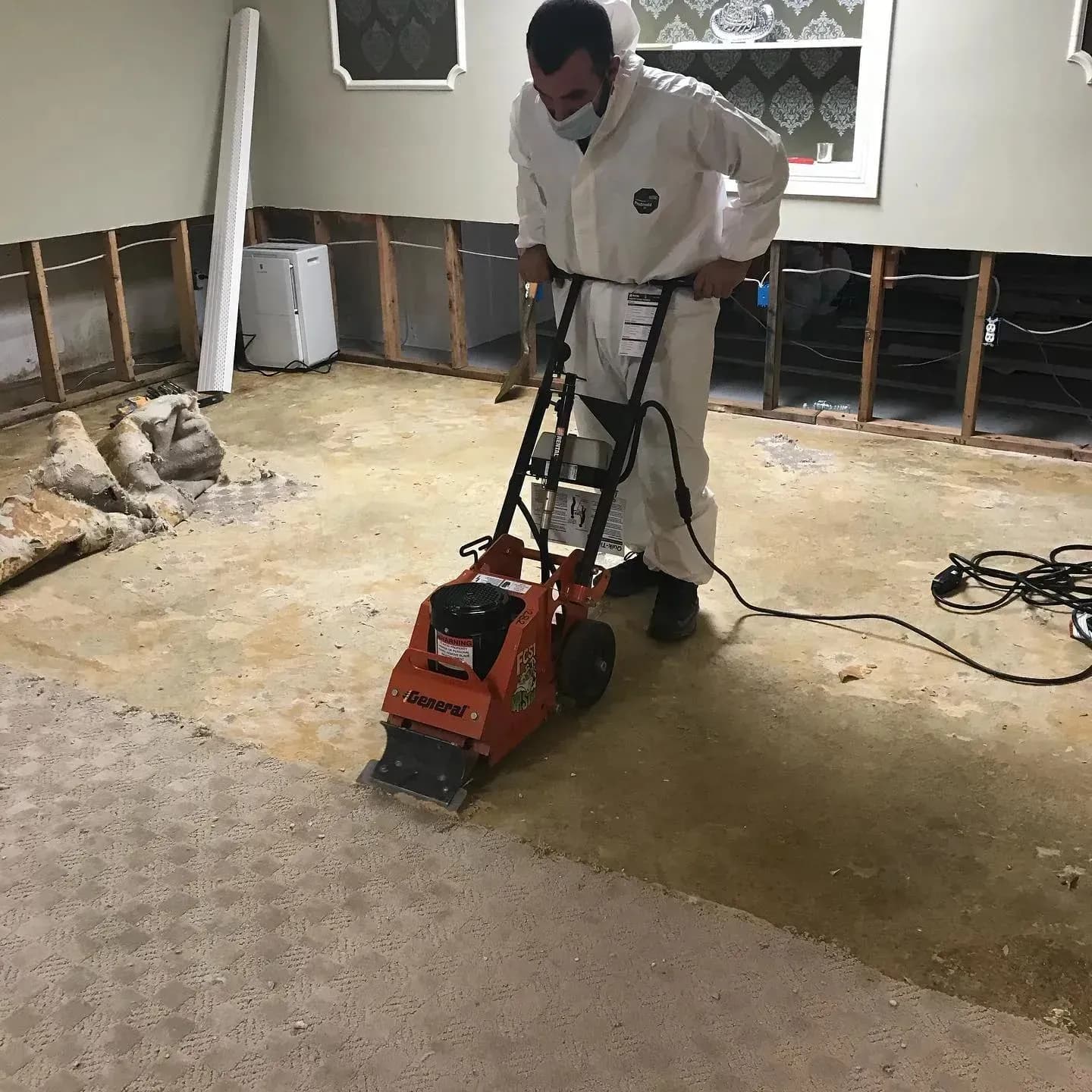 K.O.S. technician in PPE scraping a stripped floor after a sewage backup