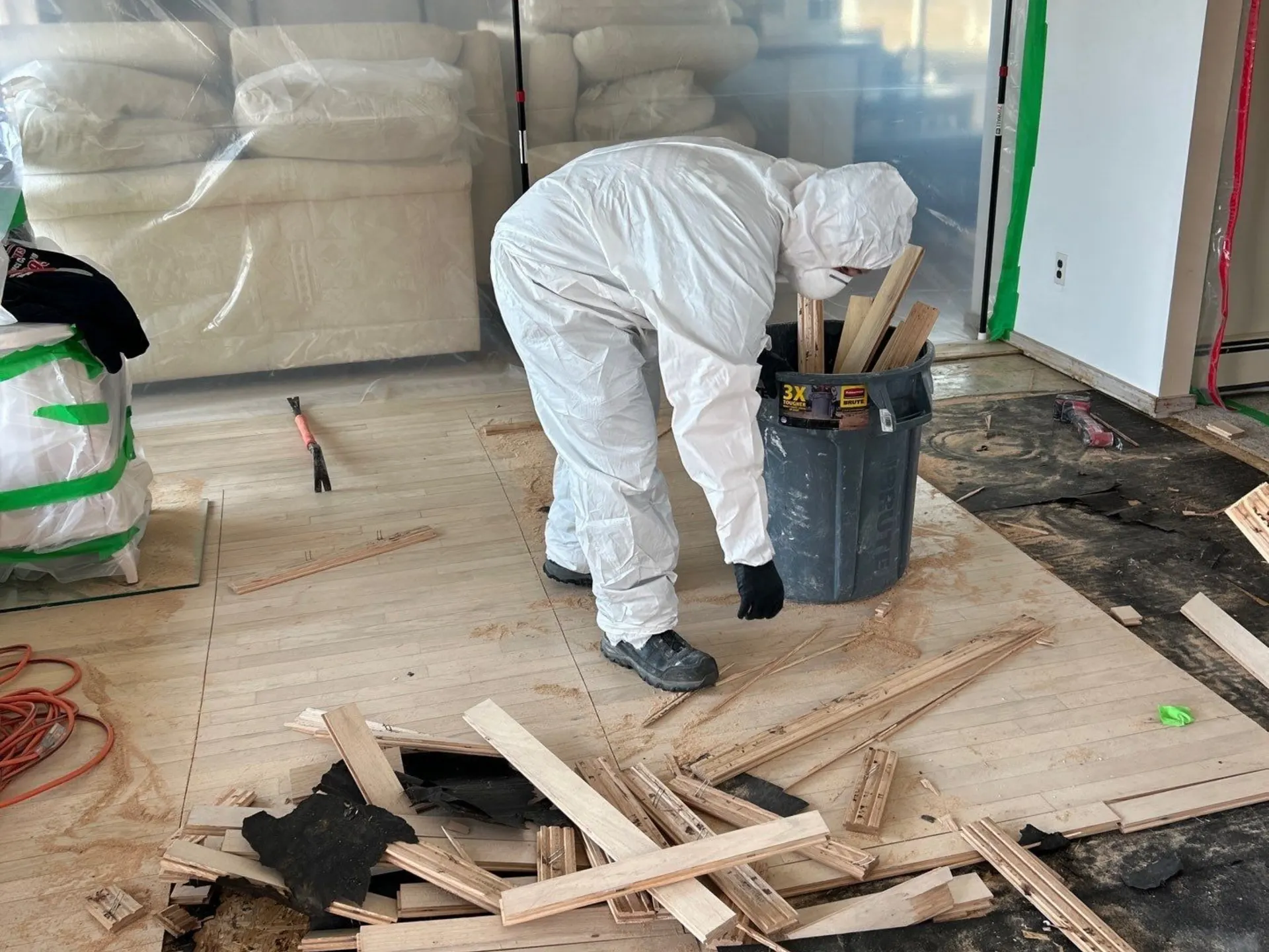K.O.S. technician in a protective suit removing water-damaged hardwood flooring in Mastic Beach