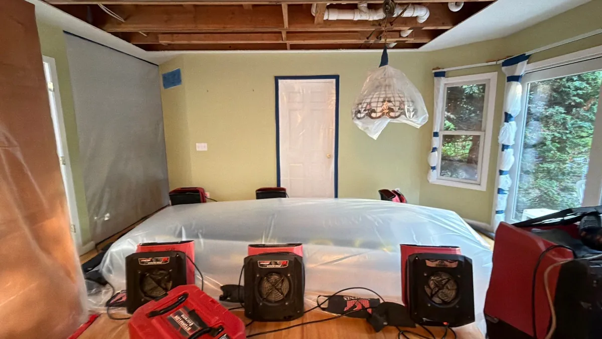 Air movers and a dehumidifier drying an East Quogue dining room with the ceiling opened and the table wrapped in plastic
