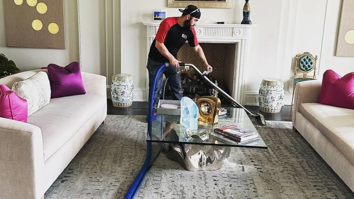K.O.S. technician cleaning carpet with a truck-mounted extraction wand in a Long Island living room
