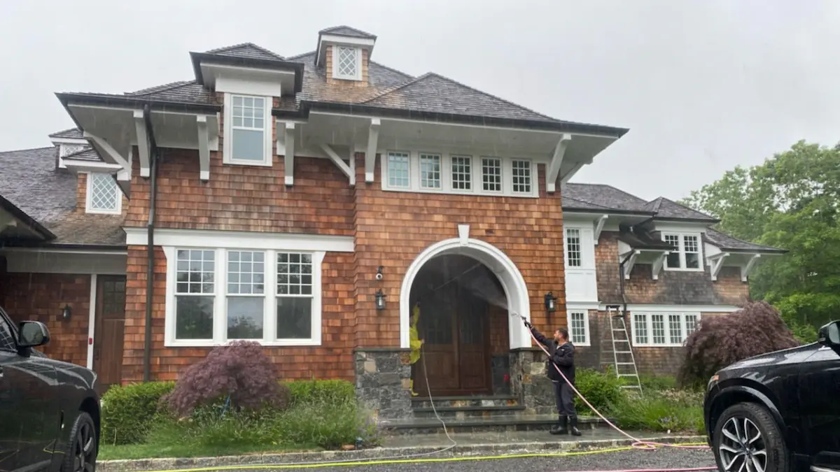 K.O.S. technician soft-washing the entrance of a brick and cedar home