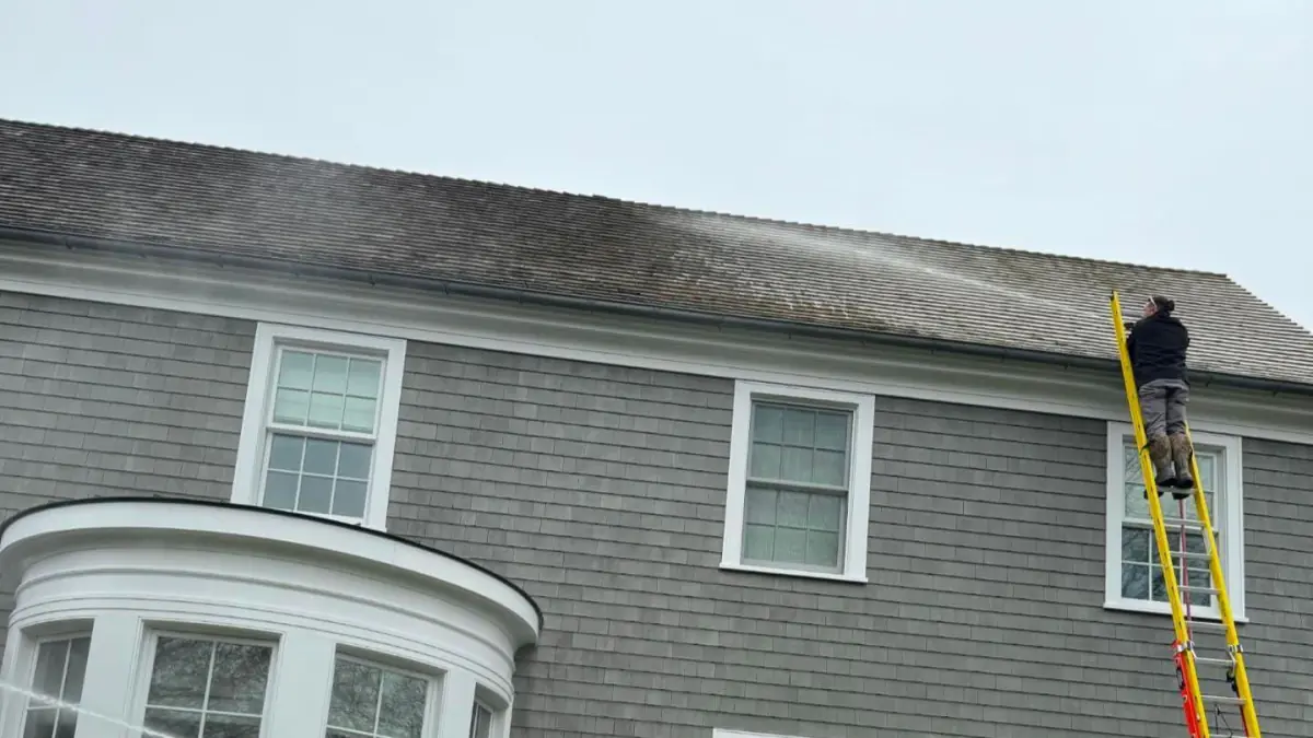 K.O.S. technician on a ladder at the roofline of a Long Island colonial