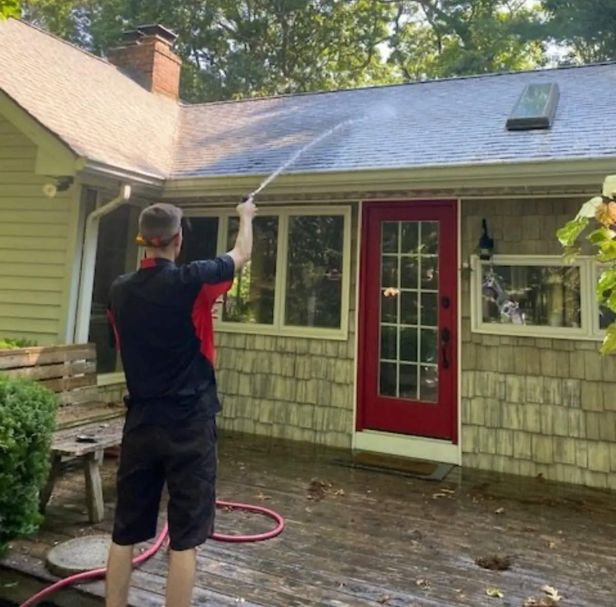 K.O.S. technician soft-washing a roof from the back deck of a Long Island home