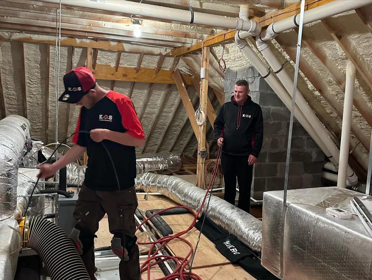 two men are working on a ventilation system in an attic .