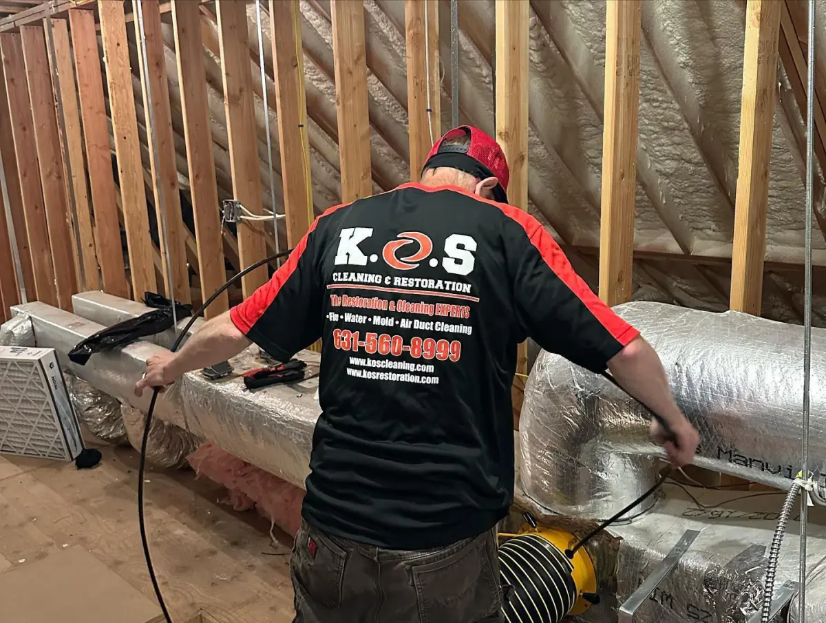 a man in a black and red shirt is working on an air duct .
