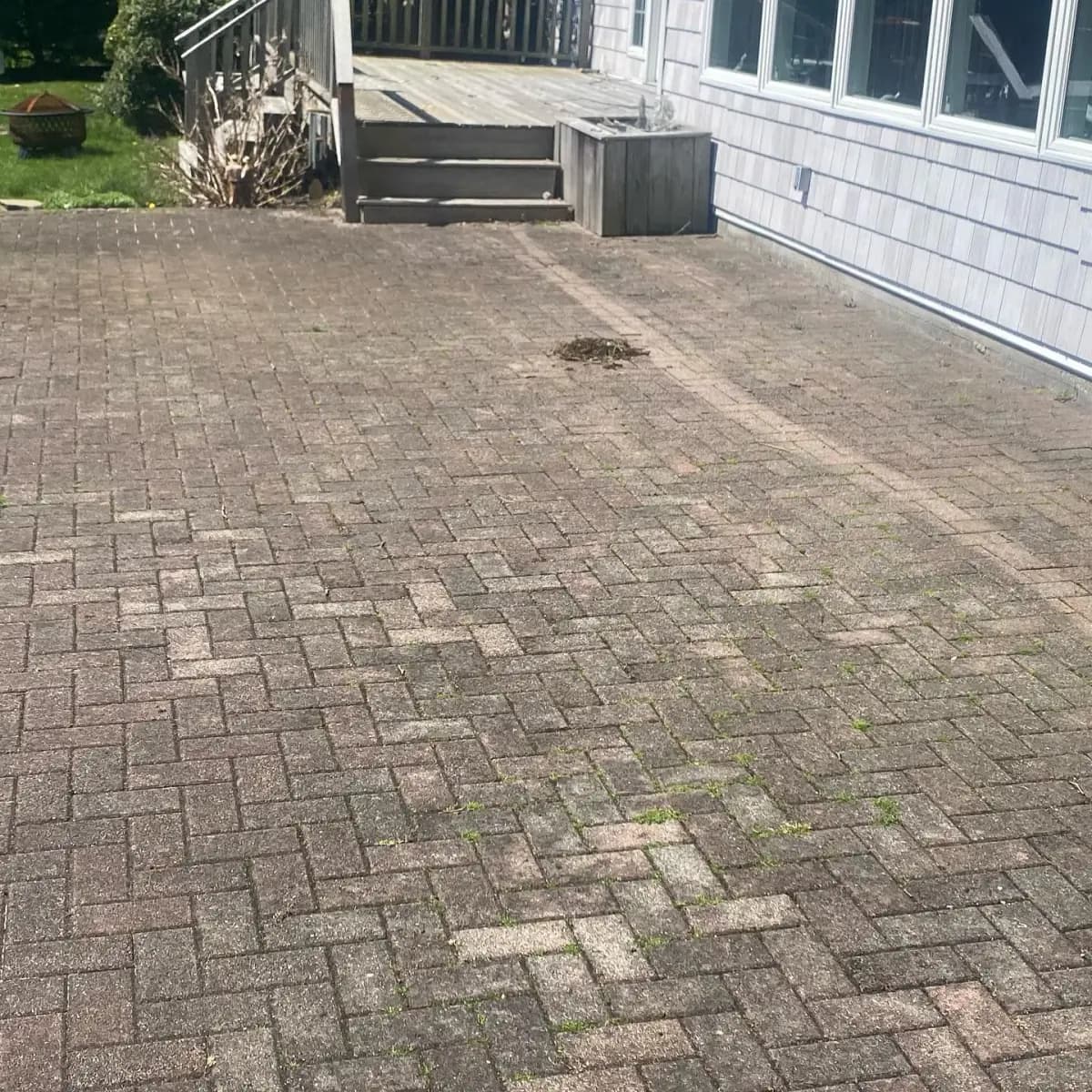 Herringbone paver patio darkened with grime, weeds in the joints, before pressure washing
