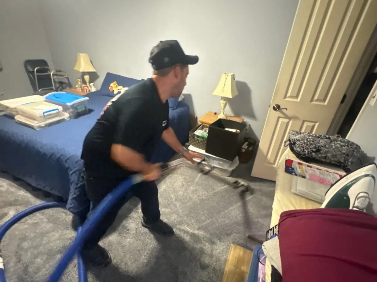 Technician extracting water from bedroom carpet with a wand