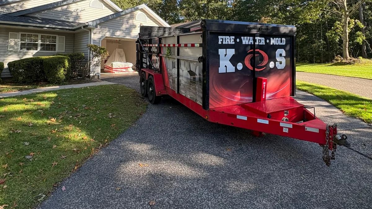 K.O.S. Restoration dump trailer parked in a Middle Island driveway with containment set up inside the open garage