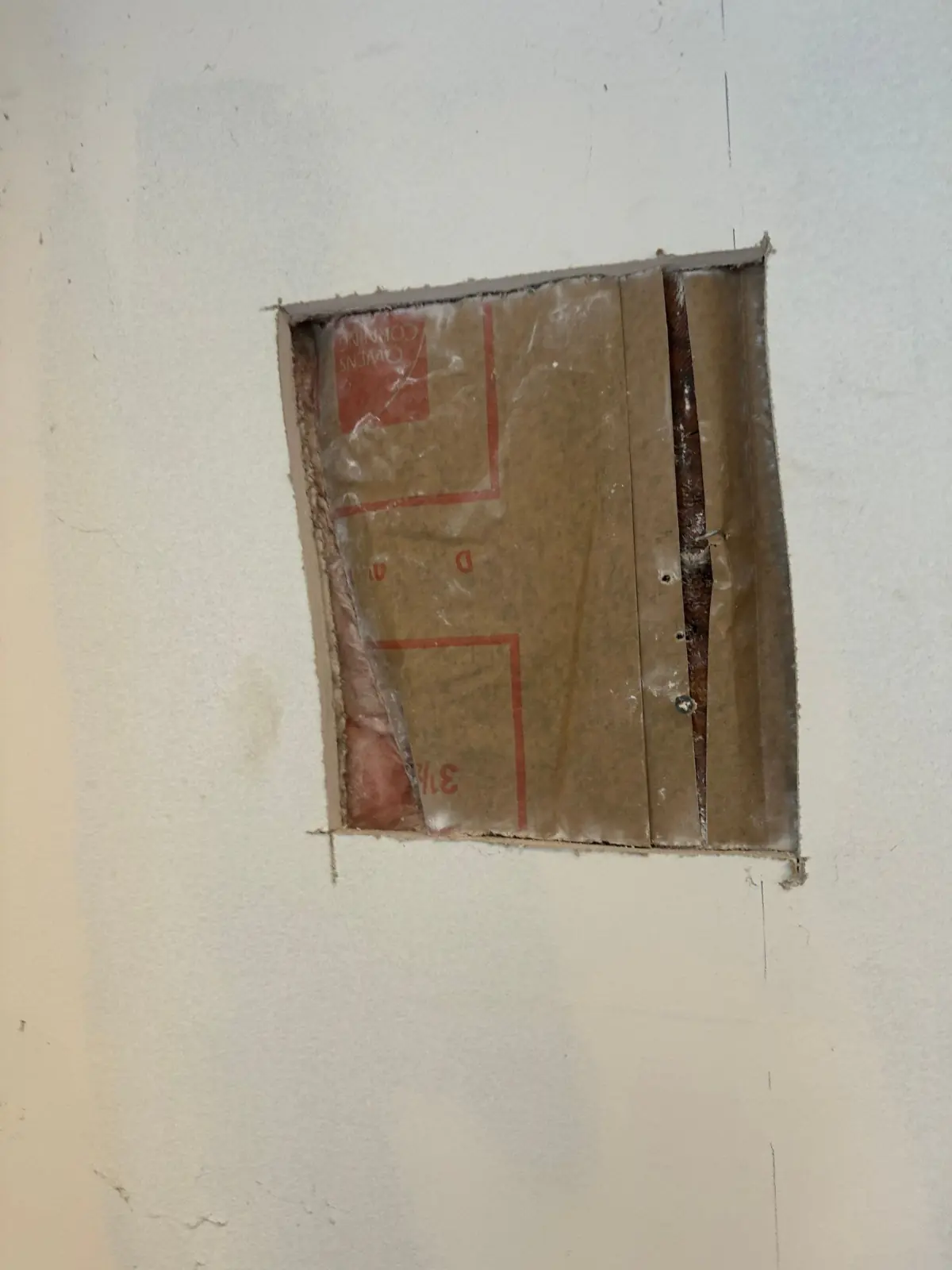 Section of drywall cut out to expose a water-damaged wall cavity