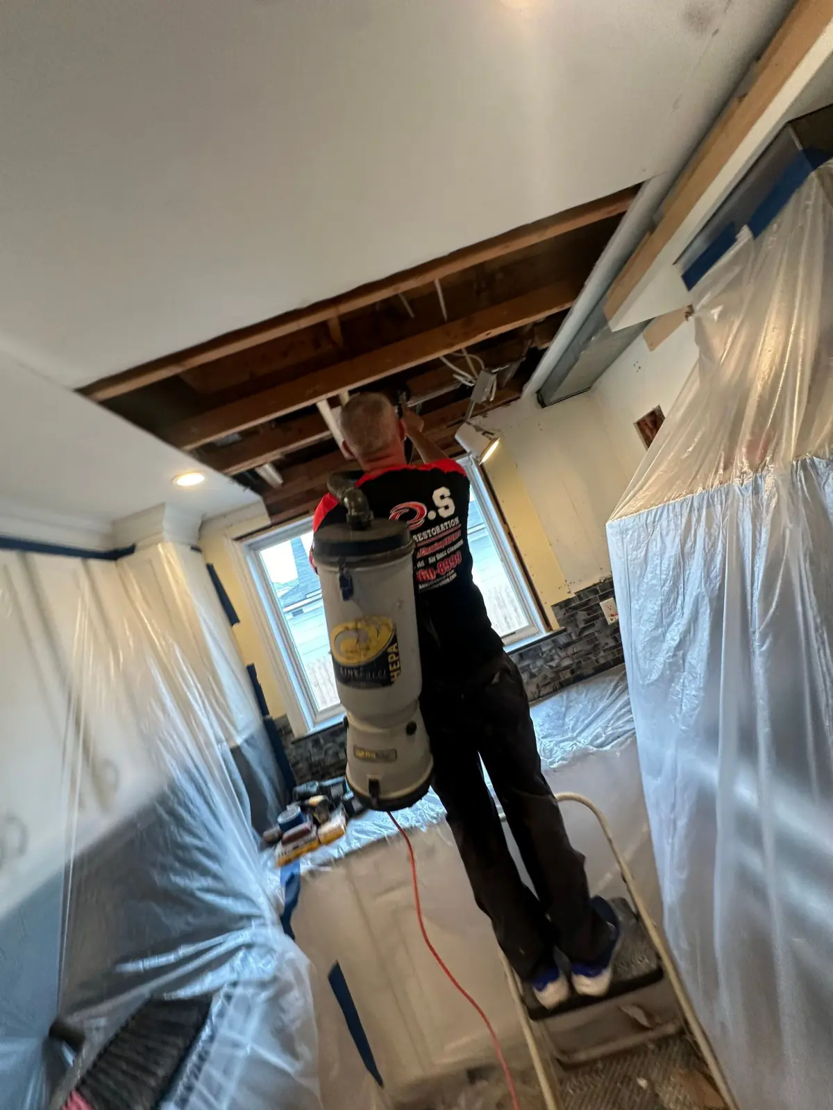 Technician HEPA-vacuuming the opened kitchen ceiling inside containment