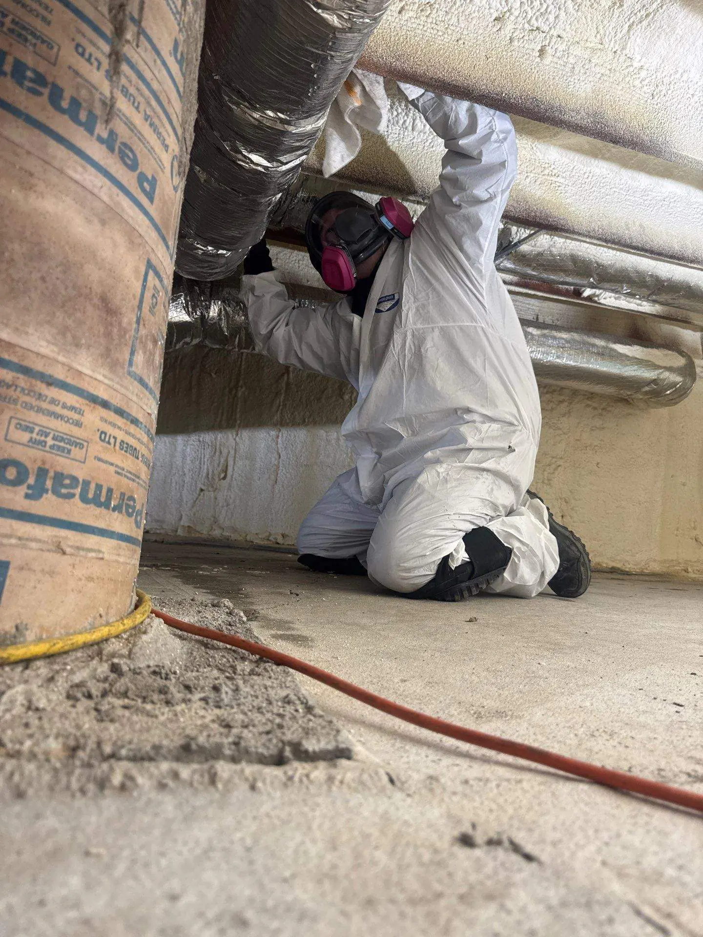 Technician in full PPE and respirator working in a crawlspace