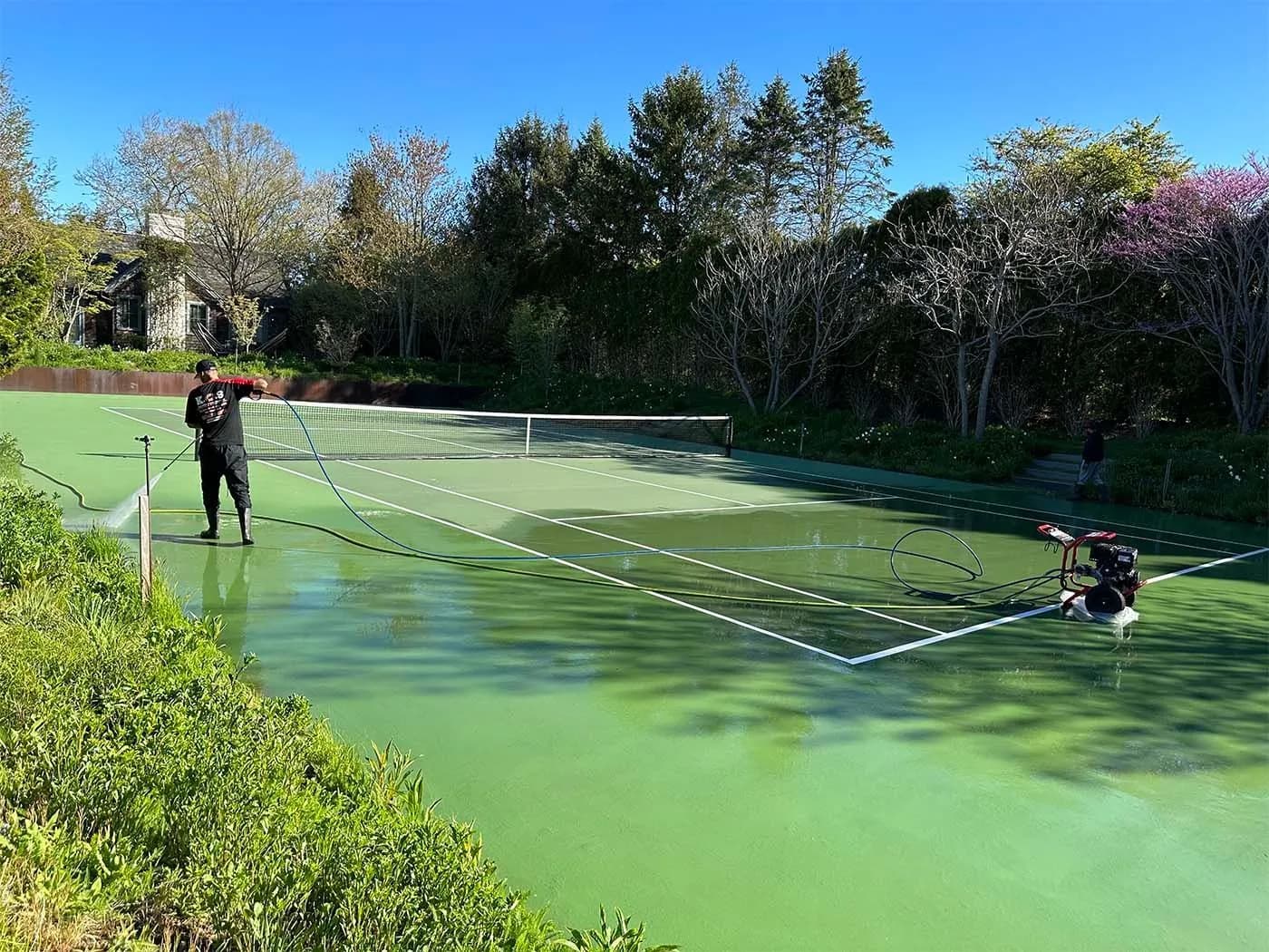 K.O.S. crew pressure-washing a green hard-surface tennis court