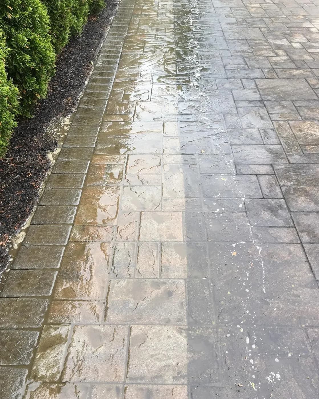 Concrete pavers mid-clean, a bright cleaned strip beside the darkened section still to go