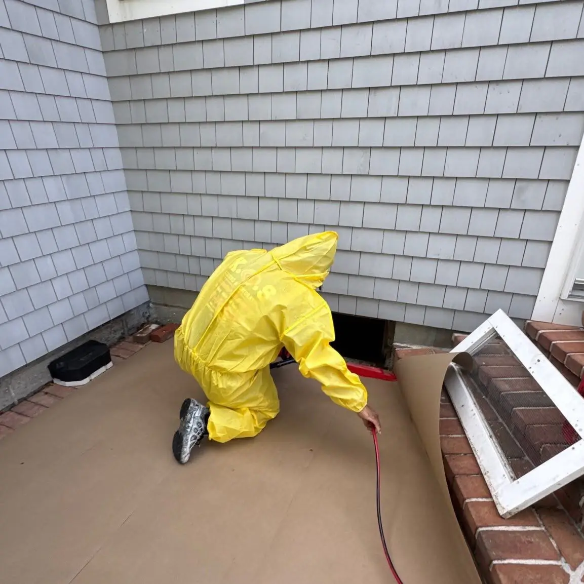 K.O.S. technician in a hazmat suit working a crawlspace access after a sewage backup