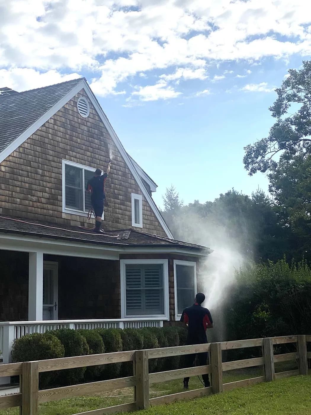 K.O.S. crew soft-washing a shingle house, one technician on a ladder at the gable
